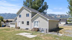 Back of house featuring a mountain view, entry steps, a lawn, and roof with shingles