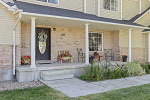 Property entrance featuring roof with shingles, covered porch, and brick siding