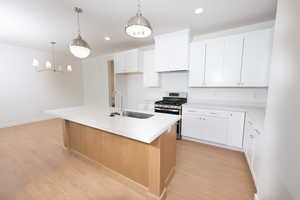 Kitchen with white cabinetry, stainless steel gas range, a kitchen island with sink, decorative light fixtures, and light wood finished floors