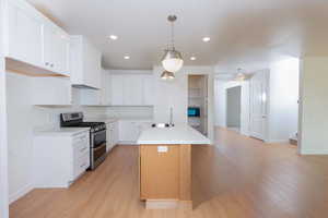 Kitchen with white cabinetry, range with two ovens, hanging light fixtures, a center island with sink, and light wood-type flooring