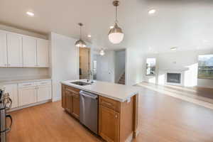 Kitchen featuring white cabinetry, decorative light fixtures, stainless steel appliances, open floor plan, and a glass covered fireplace