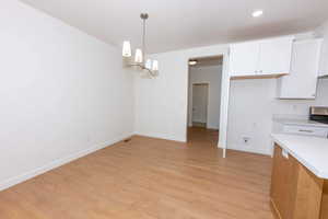 Kitchen featuring a chandelier, white cabinetry, light countertops, light wood finished floors, and hanging light fixtures