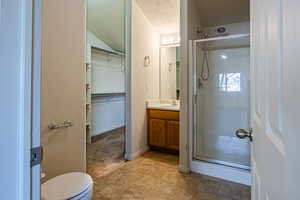 Full bathroom with vanity, a shower stall, a spacious closet, a textured ceiling, and tile patterned floors