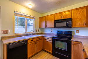 Kitchen with black appliances, a textured ceiling, light wood-style floors, and brown cabinets