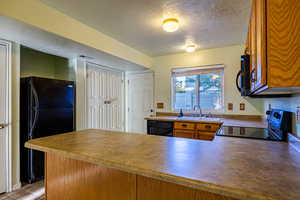 Kitchen featuring a textured ceiling, black appliances, brown cabinets, and a peninsula