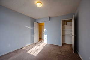 Unfurnished bedroom featuring carpet floors, a textured ceiling, and a walk in closet