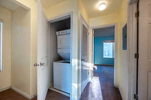 Washroom featuring estacked washer and dryer, a textured ceiling, and dark colored carpet