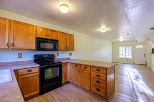 Kitchen with black appliances, a peninsula, a textured ceiling, light wood finished floors, and brown cabinetry