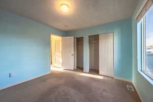 Unfurnished bedroom featuring two closets, carpet flooring, and a textured ceiling