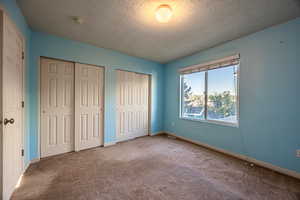 Unfurnished bedroom with two closets, carpet floors, and a textured ceiling