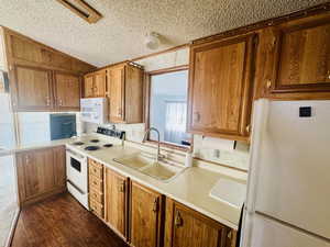 Kitchen with white appliances, light countertops, brown cabinets, dark wood-type flooring, and a textured ceiling