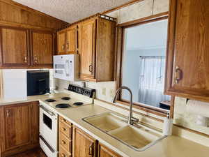 Kitchen featuring white appliances, brown cabinetry, light countertops, and a textured ceiling