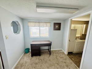 Home office featuring a textured ceiling, dark carpet, and a textured wall