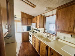 Kitchen featuring brown cabinets, white appliances, a textured ceiling, light countertops, and dark wood-style flooring