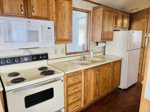 Kitchen with white appliances, brown cabinetry, dark wood-type flooring, light countertops, and a textured ceiling