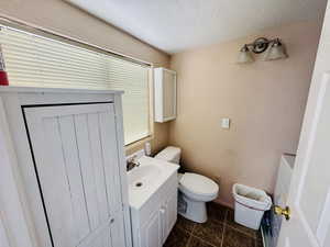 Half bathroom with a textured wall, vanity, a textured ceiling, and tile patterned floors