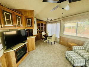 Office area with a textured ceiling, vaulted ceiling, light colored carpet, wooden walls, and ceiling fan