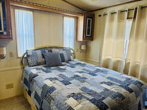 Carpeted bedroom featuring wood walls, lofted ceiling, crown molding, and a textured ceiling