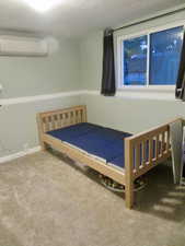 Carpeted bedroom featuring a textured ceiling and a wall mounted AC