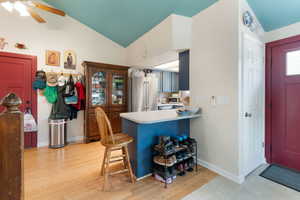 Kitchen with light wood-style flooring, freestanding refrigerator, vaulted ceiling, light countertops, and a kitchen bar