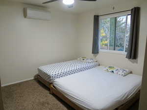 Bedroom with carpet flooring, a wall mounted AC, and a ceiling fan