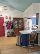 Kitchen with a kitchen breakfast bar, light countertops, freestanding refrigerator, light wood-style floors, and lofted ceiling