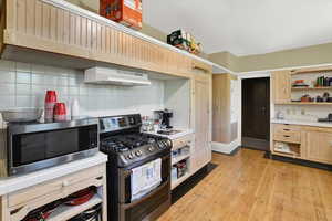 Kitchen with decorative backsplash, appliances with stainless steel finishes, open shelves, light wood-style flooring, and light brown cabinetry