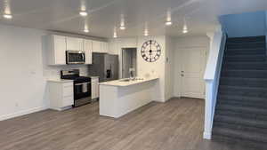 Kitchen featuring stainless steel appliances, a peninsula, white cabinetry, dark wood-type flooring, and recessed lighting