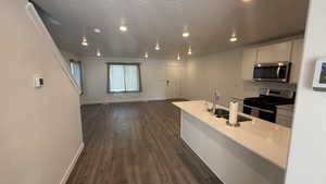 Kitchen with stainless steel appliances, open floor plan, dark wood-style floors, a textured ceiling, and white cabinetry