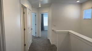 Hallway with an upstairs landing, dark carpet, and recessed lighting