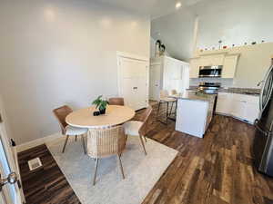 Dining room with high vaulted ceiling and dark wood-type flooring