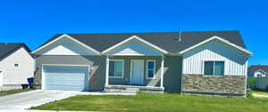 View of front facade with stone siding, a front lawn, driveway, and a 3 bay garage