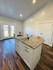 Kitchen with a kitchen bar, white cabinetry, light stone counters, dark wood finished floors, and french doors