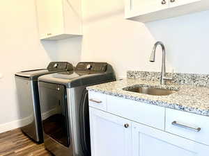 Laundry area featuring washer and dryer, cabinet space, and wood finished floors and a sink with granite countertop. cabinets above and hanging rod.