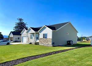 View of home's exterior featuring board and batten siding, stone siding, a lawn, driveway, and a garage. Faces South.