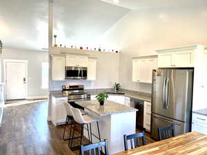 Kitchen featuring appliances with stainless steel finishes, dark wood-style floors, a bar / island center  and granite stone counters