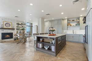 Kitchen with open shelves, light countertops, recessed lighting, a stone fireplace, and decorative backsplash