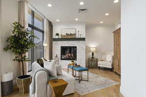 Living room with wood finished floors, recessed lighting, a stone fireplace, and ornamental molding