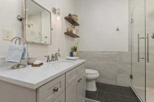 Full bathroom featuring tile walls, vanity, a shower stall, tile patterned floors, and wainscoting