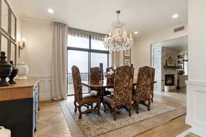 Dining space with ornamental molding, a stone fireplace, a chandelier, wainscoting, and recessed lighting