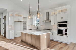 Kitchen with glass insert cabinets, backsplash, decorative light fixtures, wall chimney range hood, and lofted ceiling