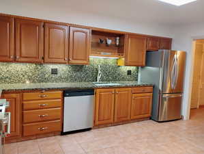 Kitchen featuring decorative backsplash, stainless steel appliances, brown cabinetry, and dark stone counters