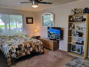 Bedroom with light carpet, ornamental molding, and ceiling fan