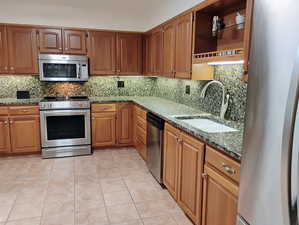 Kitchen featuring light tile patterned flooring, stainless steel appliances, stone counters, and tasteful backsplash