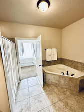 Ensuite bathroom with a textured ceiling, a garden tub, light tile patterned floors, and a stall shower