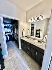 Bathroom with a spacious closet, double vanity, and light tile patterned floors