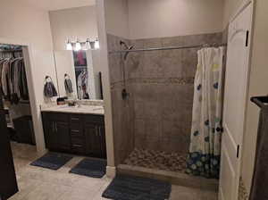 Full bathroom featuring tiled shower, tile patterned flooring, a spacious closet, and double vanity