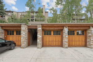 View of front of property featuring stone siding, concrete driveway, a garage, and a chimney