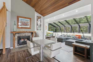 Living room with lofted ceiling, a tiled fireplace, a sunroom, wood ceiling, and dark wood-style floors