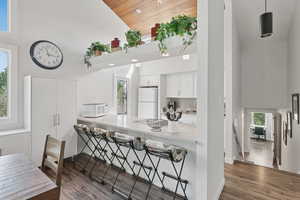 Kitchen featuring high vaulted ceiling, white appliances, white cabinetry, a breakfast bar, and dark wood-style floors